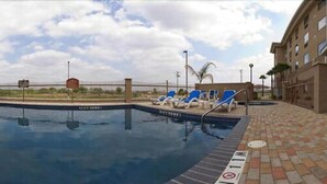 A swimming pool with lounge chairs, a fenced area, and a building in the background. - Holiday Inn Express Hotel & Suites Laredo-Event Center Area by IHG (Laredo)