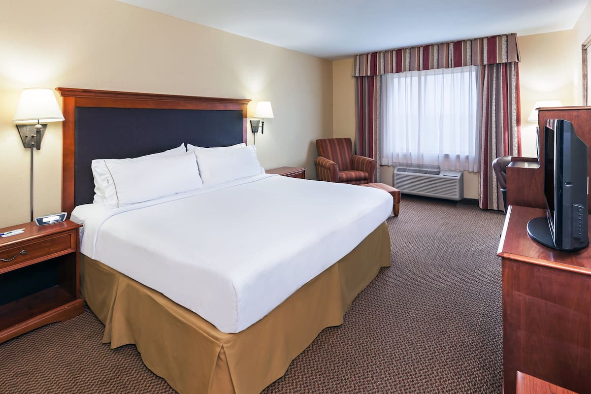 A hotel room with a large bed, a desk with a flat-screen TV, a chair, and a window with curtains.