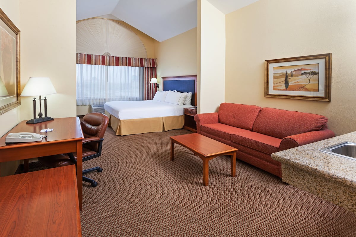 A hotel room with a bed, a red sofa, a wooden desk, a lamp, and a painting on the wall.