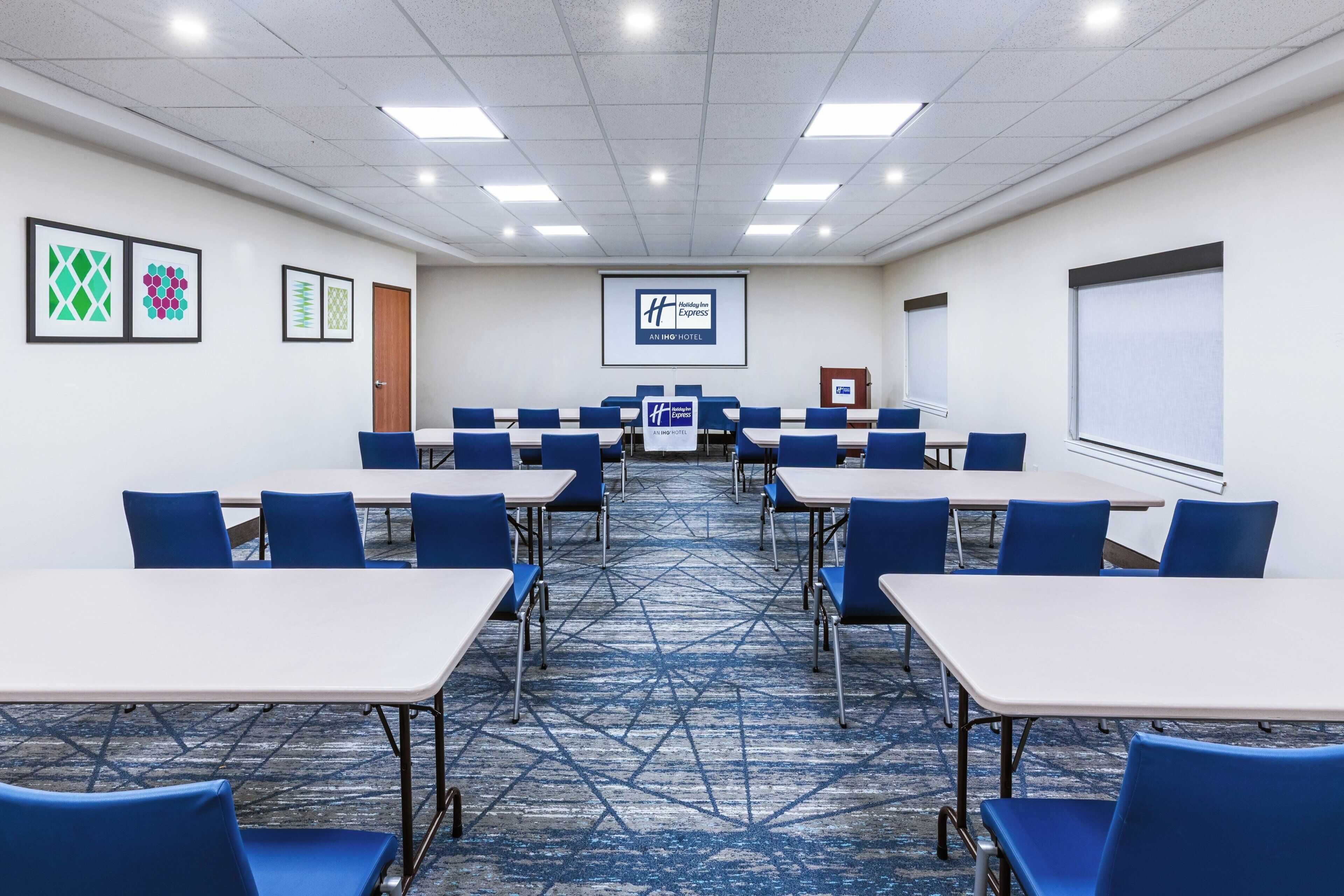 A conference room with tables and chairs, a projector screen, and a carpeted floor.