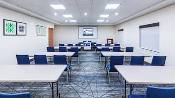 A conference room with tables and chairs, a projector screen, and a carpeted floor.