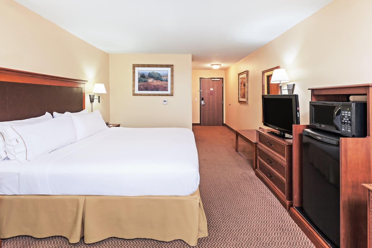 A hotel room with a large bed, a television, a microwave, and a dresser.