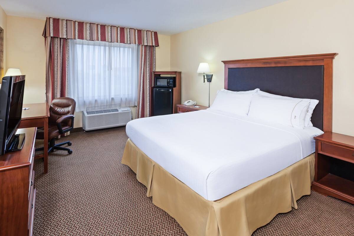 A hotel room with a large bed, a desk with a computer, a chair, a desk lamp, a telephone, and a microwave.