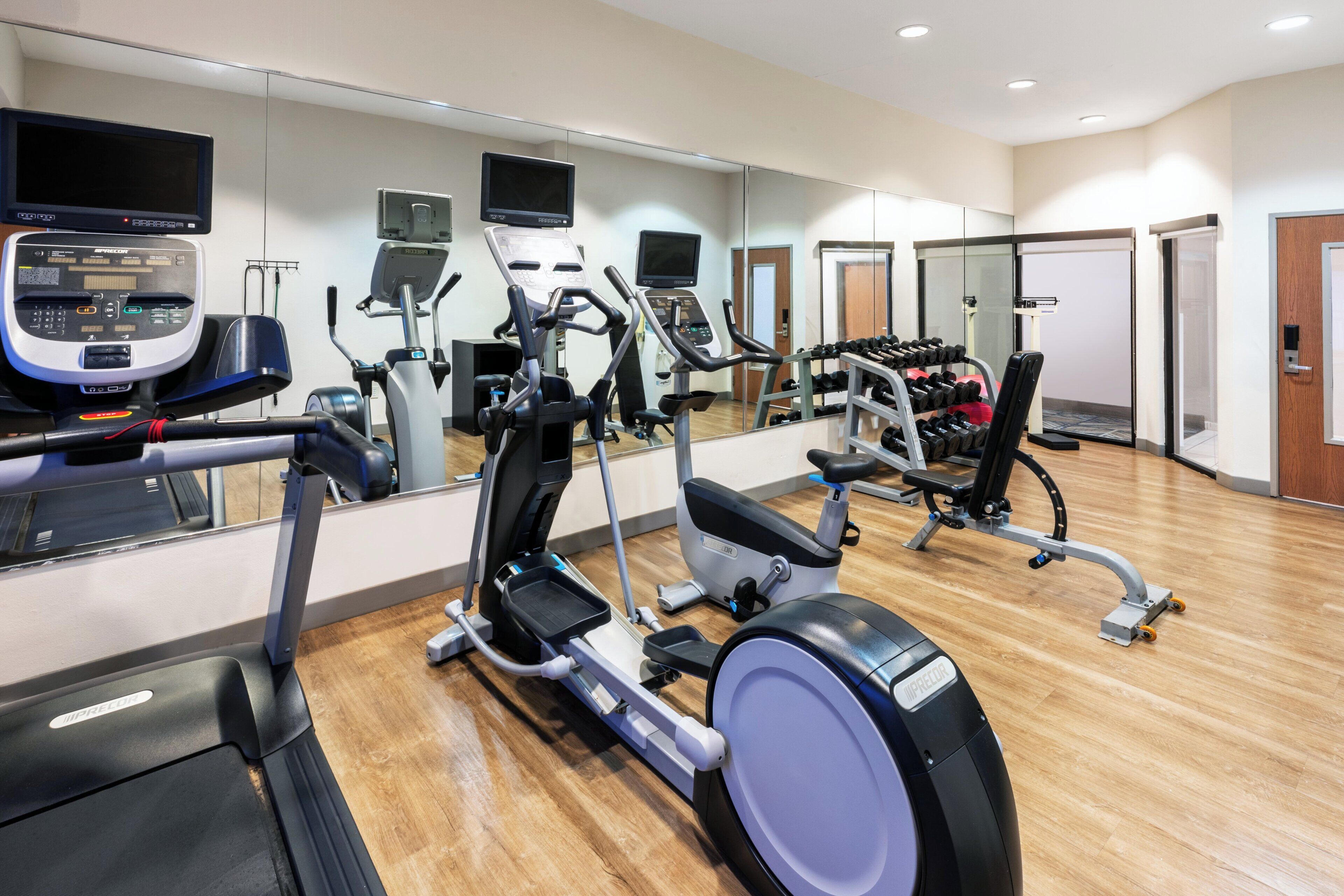 Ein Fitnessstudio mit Laufbändern, Kraftbänken und einem Spiegel, der die Geräte reflektiert.