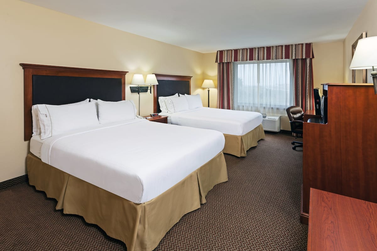 A hotel room with two beds, a desk, a chair, and a window with curtains.