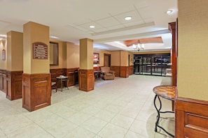 A spacious lobby with a high ceiling, a central seating area, and a sign indicating amenities like an elevator, restrooms, ice & vending, outdoor pool, and fitness center.