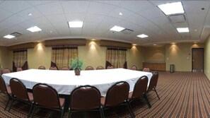 Un salón de conferencias con una gran mesa ovalada, sillas marrones y una planta en maceta.