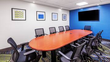 A conference room with a long table and six chairs, a flat-screen TV on the wall, and framed artwork on the wall.