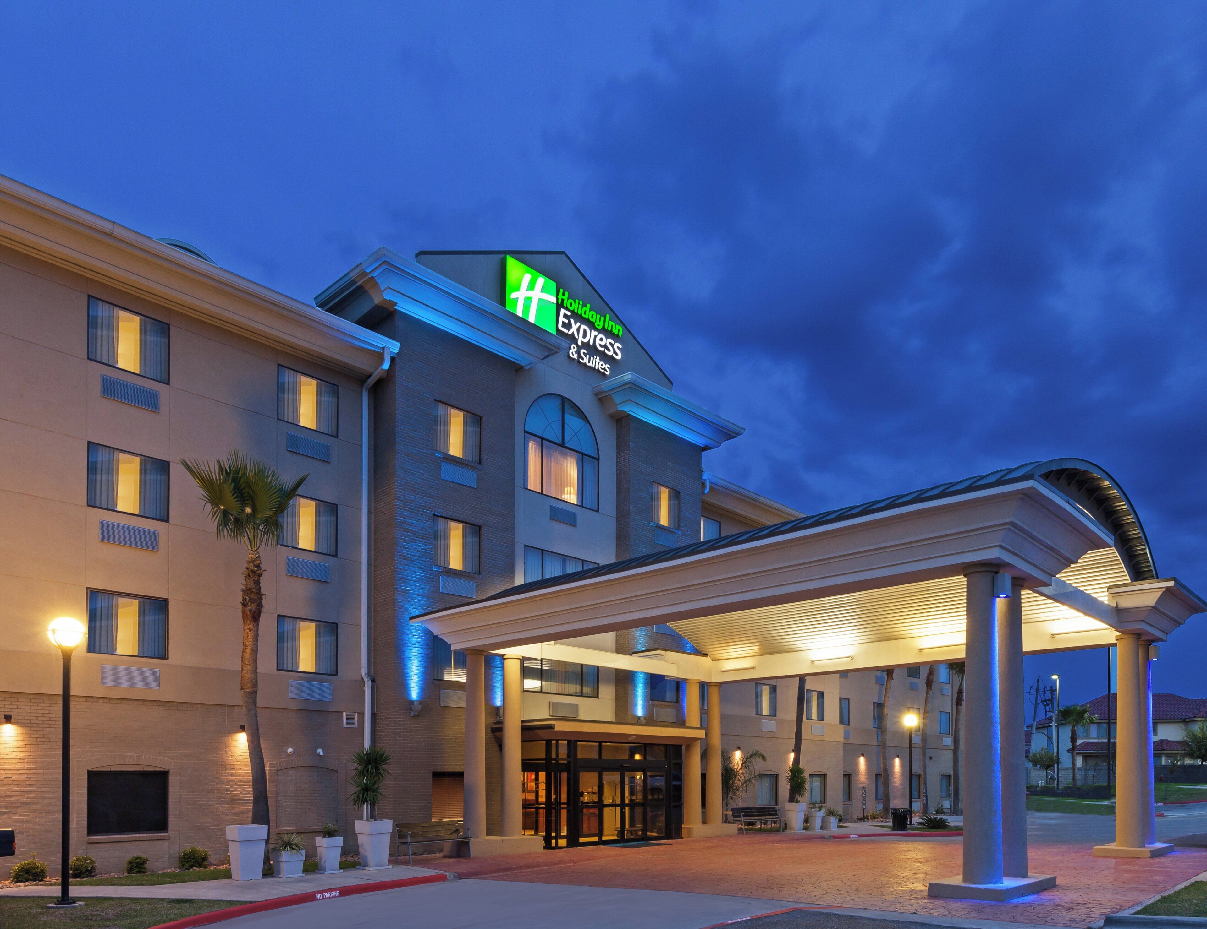 A hotel with a modern design, featuring a prominent green and white sign, a covered entrance, and a well-lit facade.