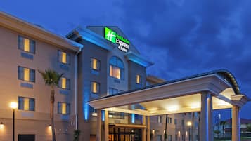 A hotel with a modern design, featuring a prominent green and white sign, a covered entrance, and a well-lit facade.