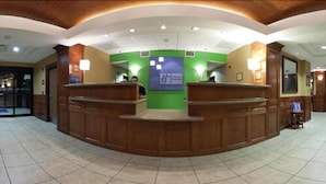 A reception area with a curved wooden reception desk, a green wall with a sign, and a tiled floor. - Holiday Inn Express Hotel & Suites Laredo-Event Center Area by IHG (Laredo)