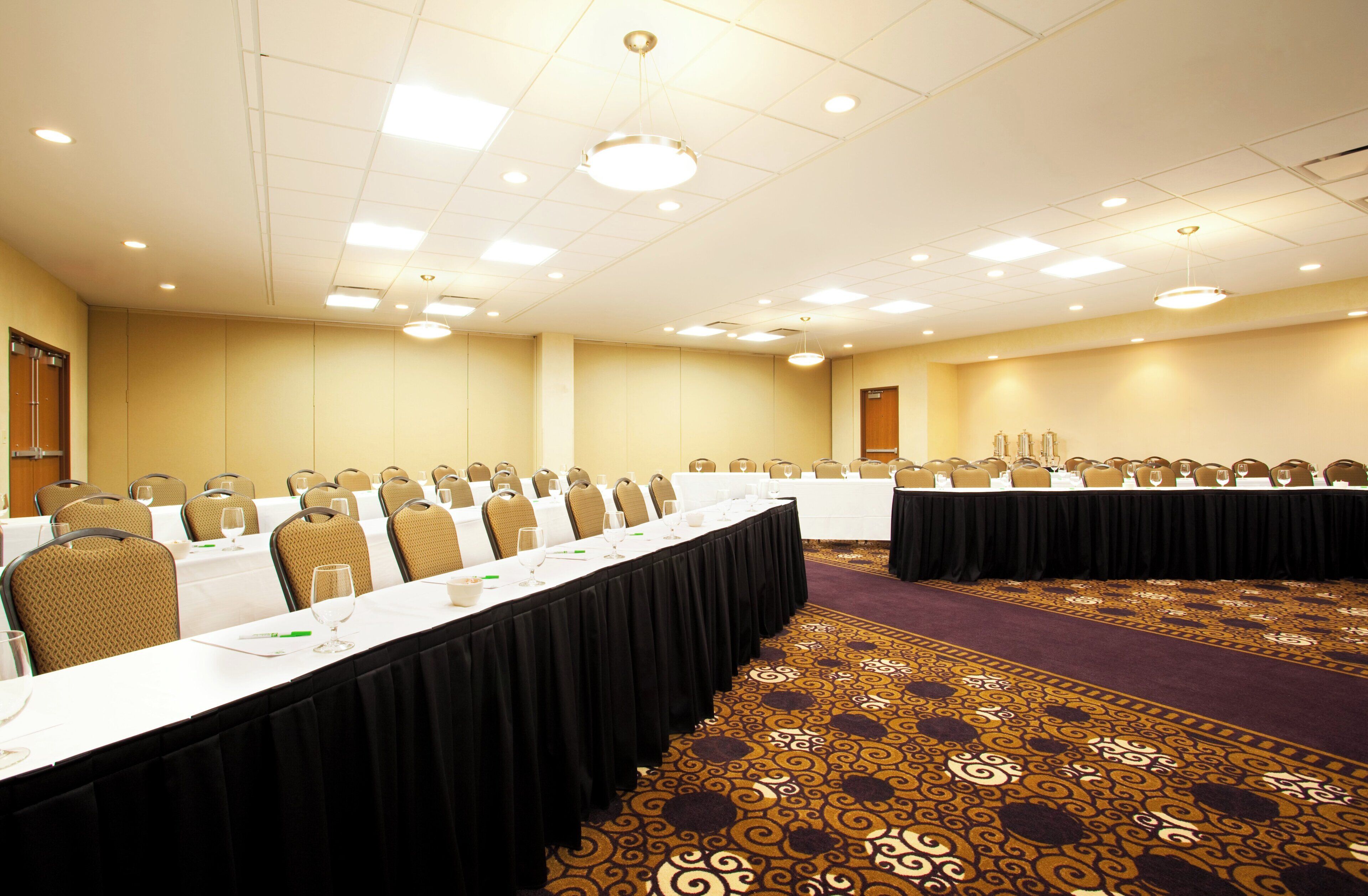 A conference room with long tables, chairs, and a patterned carpet.