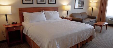 A hotel room with a large bed, a nightstand, a desk, a chair, and two lamps.