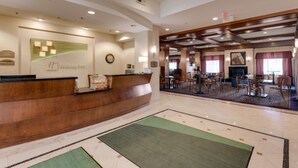 A hotel reception area with a wooden reception desk, a clock, and a framed welcome sign. There are multiple dining tables and chairs in the background. - Holiday Inn Battle Creek by IHG (Battle Creek)