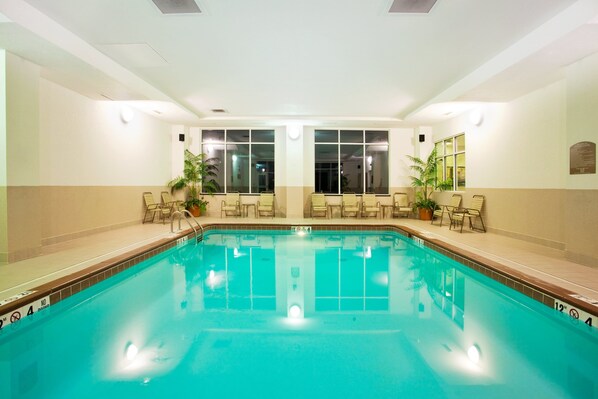 Una piscina interior con agua cristalina, rodeada de sillones de descanso y plantas en macetas.