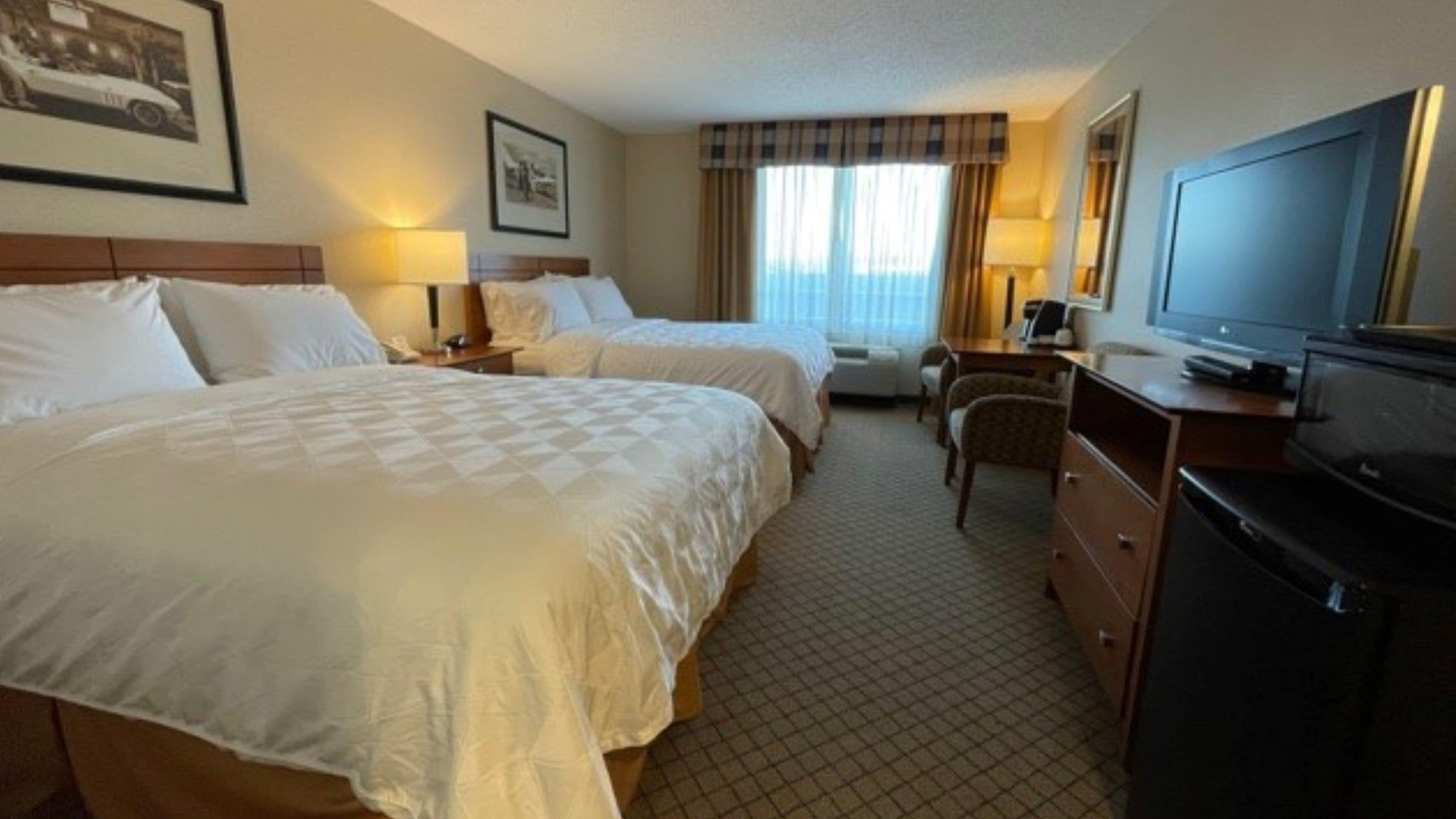 A hotel room with two beds, a desk, a chair, a television, and a window with curtains.