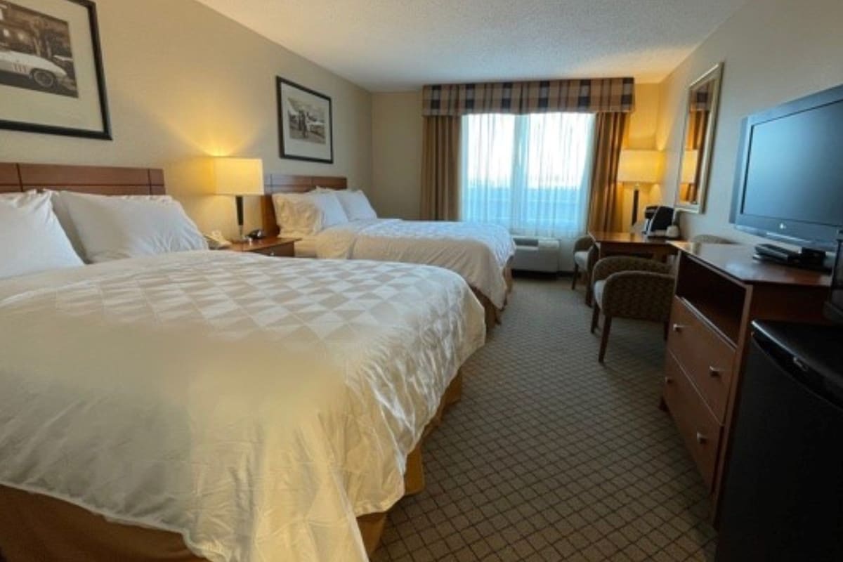 A hotel room with two beds, a desk, a chair, a television, and a window with curtains.