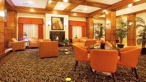 A hotel lobby with a patterned carpet, orange seating, a fireplace, and a large mirror. - Holiday Inn Battle Creek by IHG (Battle Creek)