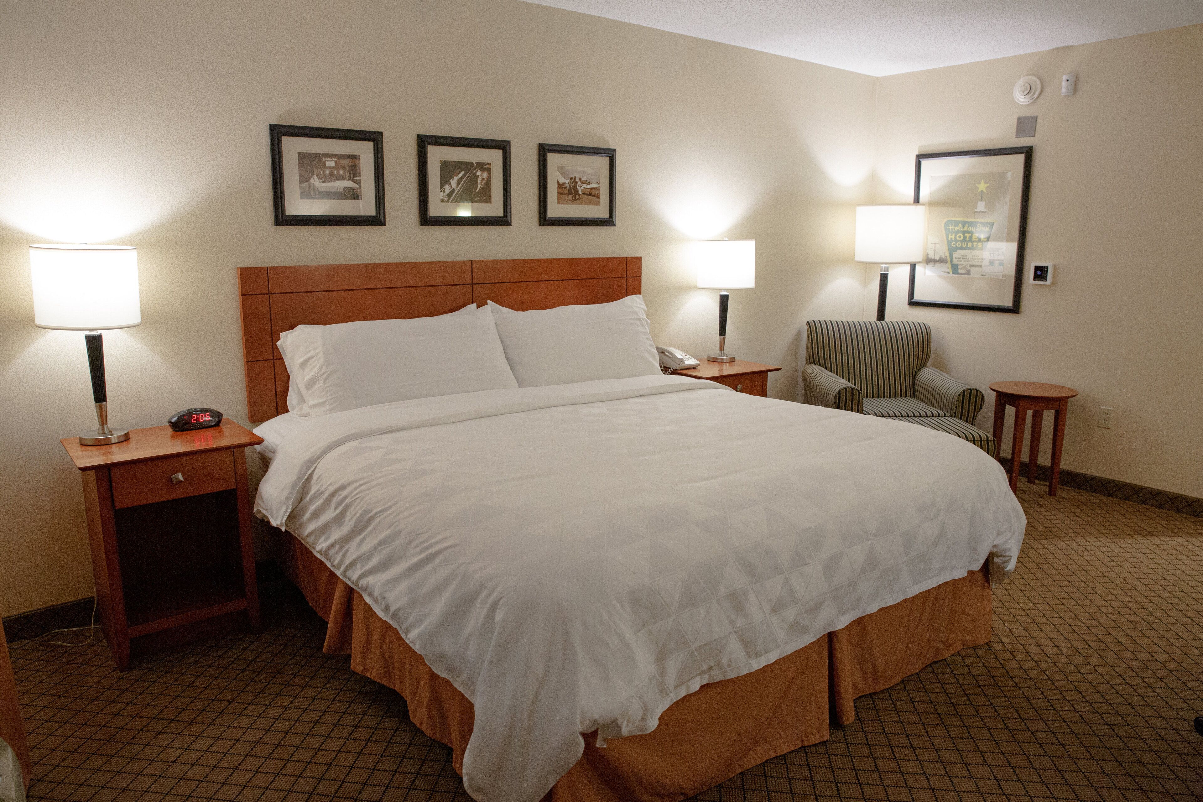 A hotel room with a large bed, two bedside tables with lamps, a chair, and framed pictures on the wall.