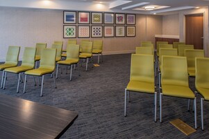 A conference room with rows of yellow chairs, a long table, and a carpeted floor.
