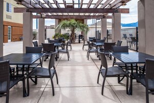 Un patio al aire libre con varias mesas y sillas, una pérgola en lo alto y una palmera.