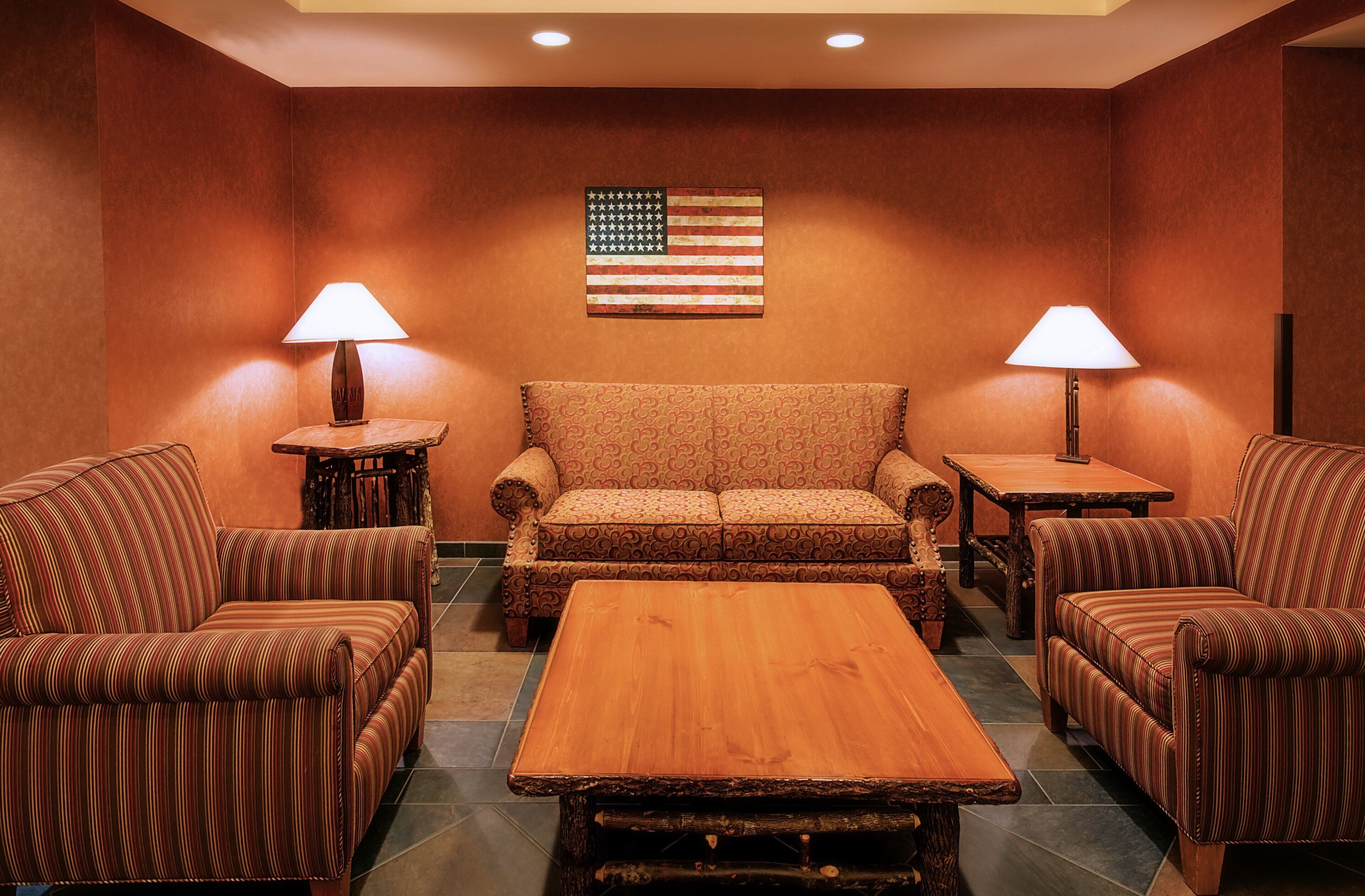 A hotel room with a sofa, two armchairs, a coffee table, and two lamps. An American flag is displayed on the wall.