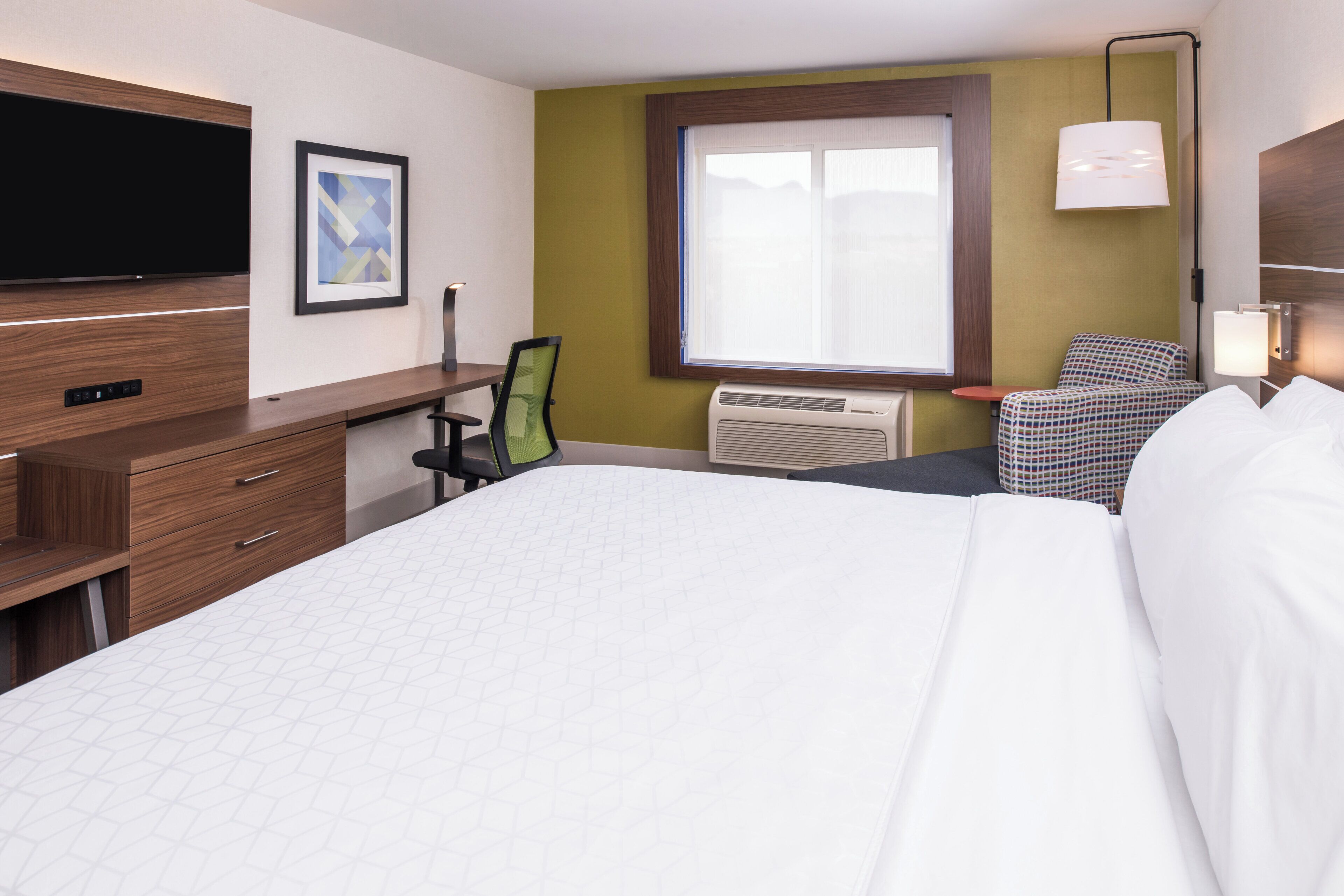 A hotel room with a bed, a desk, a chair, a television, and a window.