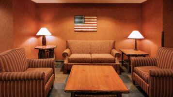 Una habitación con un sofá, dos sillones, una mesa de centro de madera y dos lámparas. Se exhibe una bandera estadounidense en la pared.