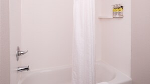 Eine weiße Badewanne mit Duschvorhang, Handtuch und Ablage für Pflegeprodukte.