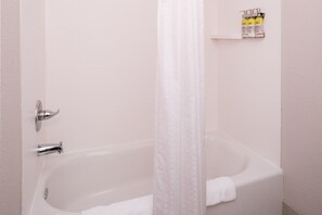 Una bañera blanca con cortina de ducha, una toalla y un estante con artículos de aseo.