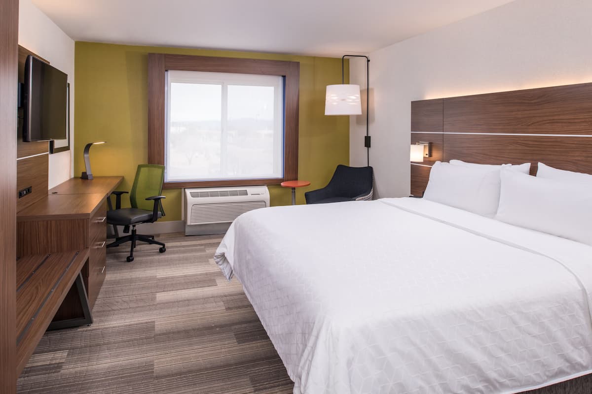 A hotel room with a bed, desk, chair, TV, window, and lamp.