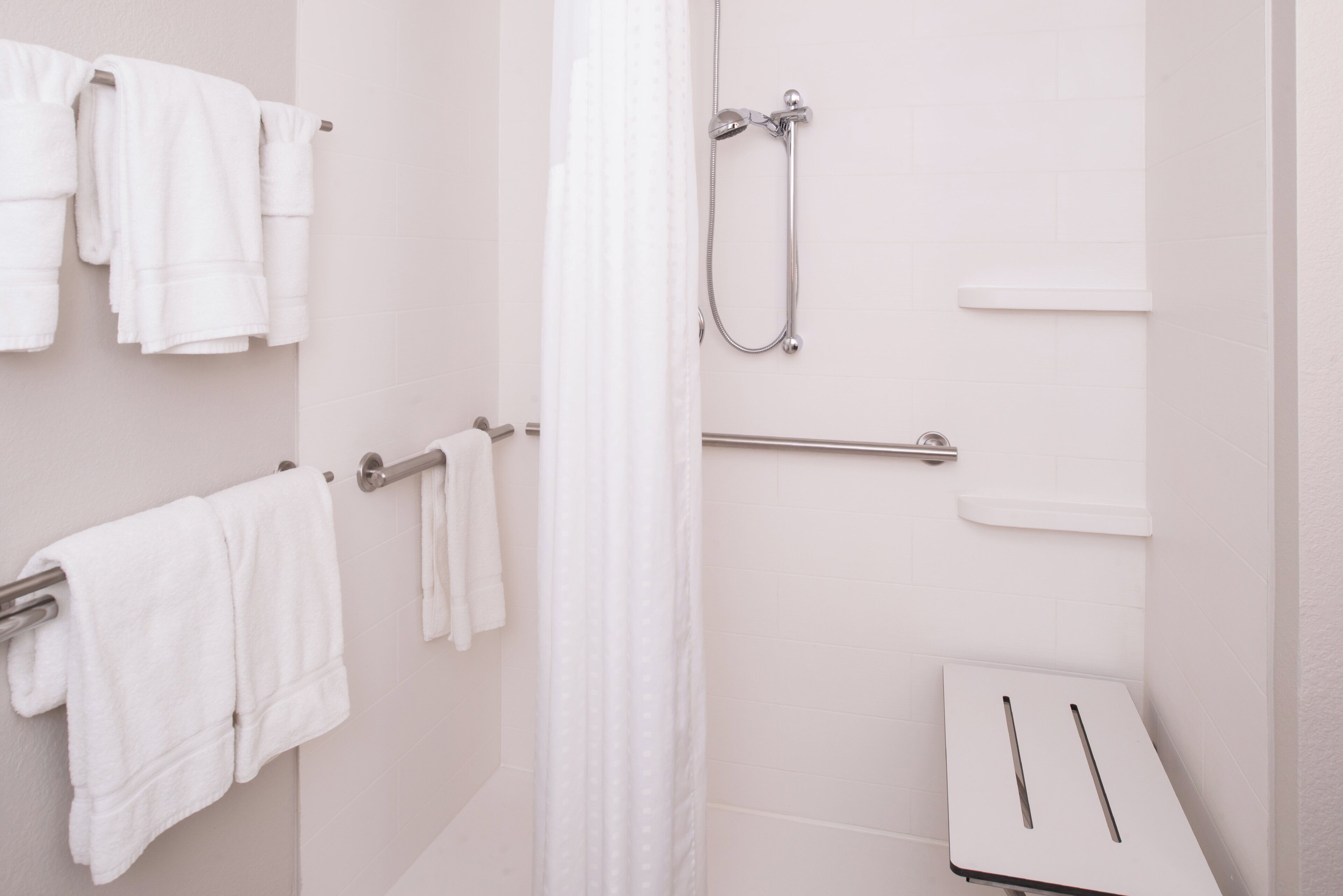 Ein Badezimmer mit weißen Fliesen, einer Dusche inklusive Handbrause und zwei Handtuchhaltern mit weißen Handtüchern.
