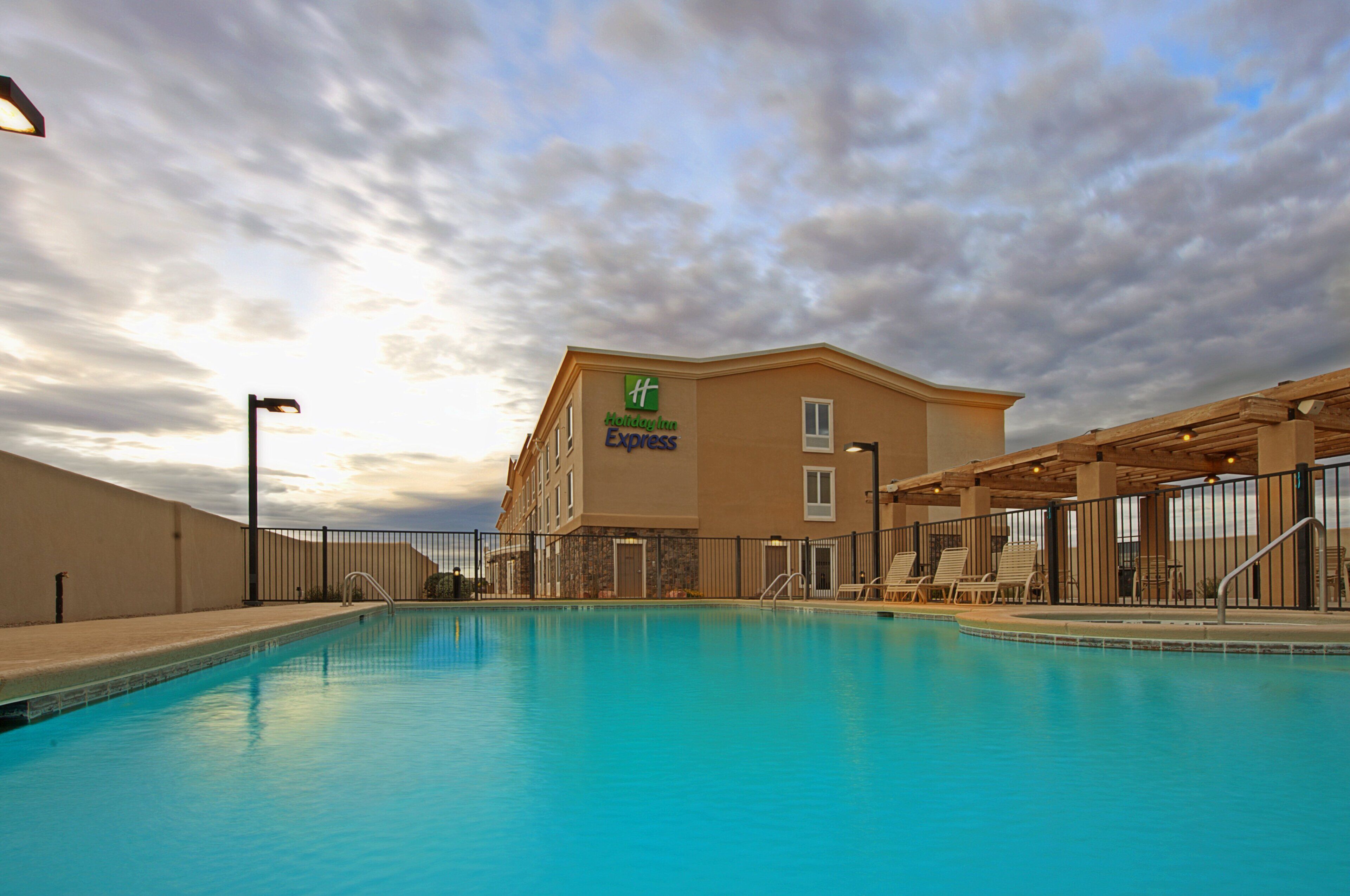 A hotel with a swimming pool, outdoor lounge chairs, and a covered patio area.