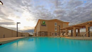 A hotel with a swimming pool, outdoor lounge chairs, and a covered patio area.
