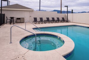 A swimming pool with a hot tub, lounge chairs, and a view of mountains.