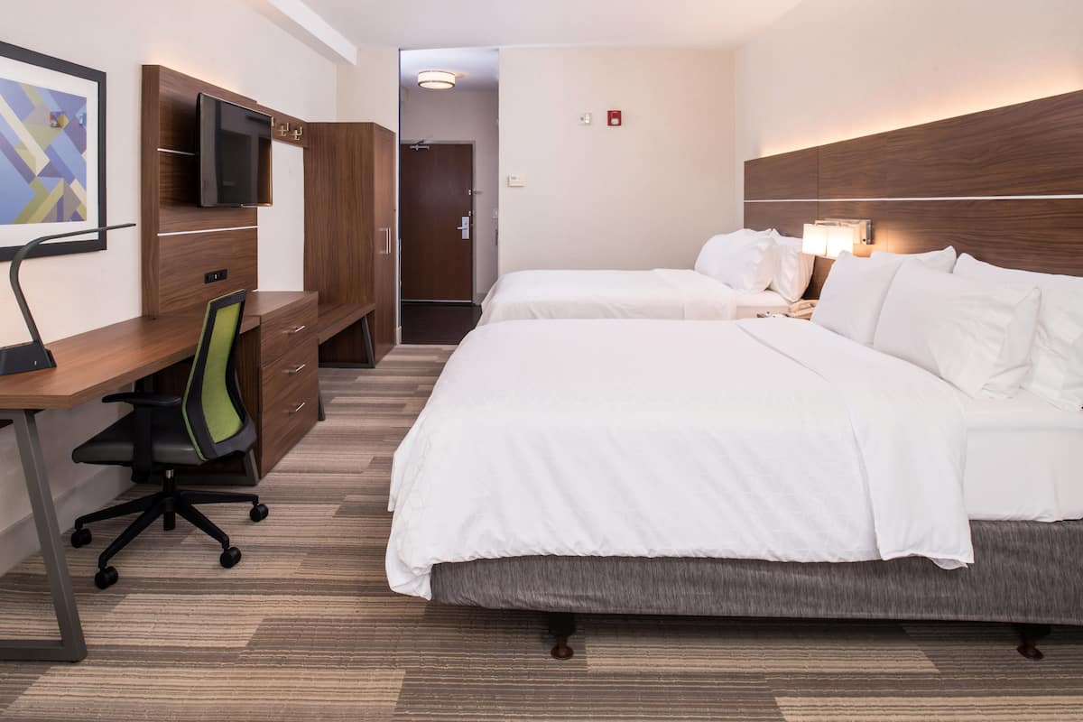 A hotel room with a desk, two beds, a TV, and a door leading to another room.