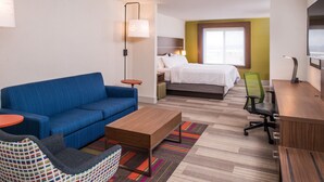 Ein Hotelzimmer mit einem blauen Sofa, einem Holztisch, einem grünen Bürostuhl, einem Bett mit weißer Bettwäsche und einem an der Wand befestigten Fernseher.