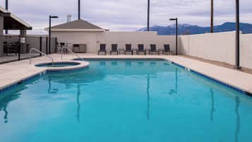 A swimming pool with a hot tub, lounge chairs, and a view of mountains.
