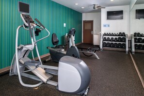 A gym with treadmills, an elliptical, a bench press, and a rack of dumbbells.