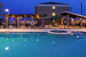 Una piscina con jacuzzi, rodeada de mobiliario exterior y una zona cubierta con iluminación.