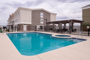 A swimming pool with a pergola and outdoor seating area, surrounded by a fence.