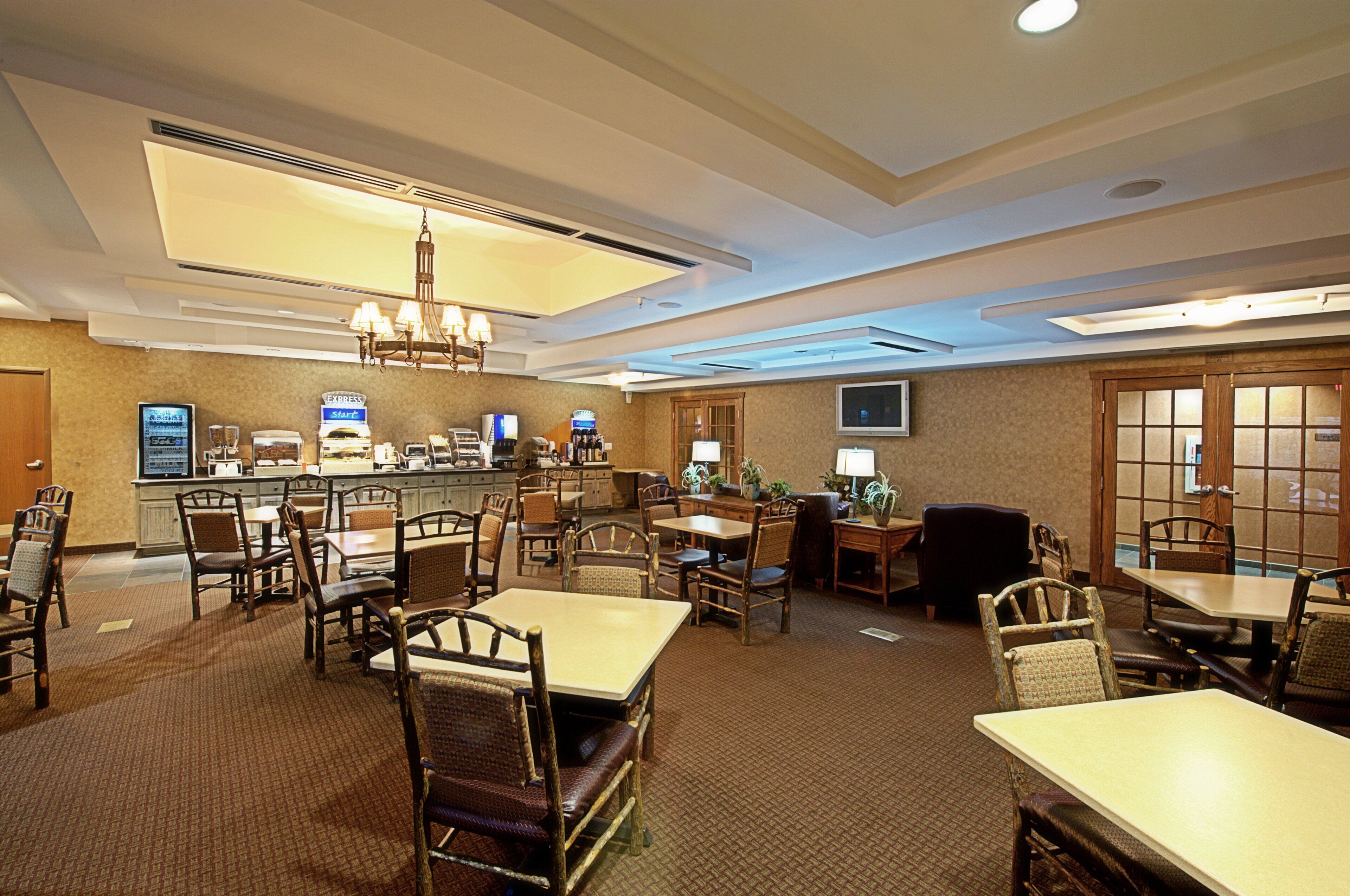 Ein Restaurantbereich in einem Hotel mit mehreren Tischen, Stühlen und einer Bar, einschließlich eines Kronleuchters.