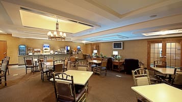 Ein Restaurantbereich in einem Hotel mit mehreren Tischen, Stühlen und einer Bar, einschließlich eines Kronleuchters.