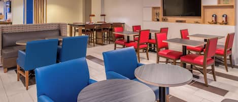 A hotel lobby with seating areas, a flat-screen TV, and a coffee machine.