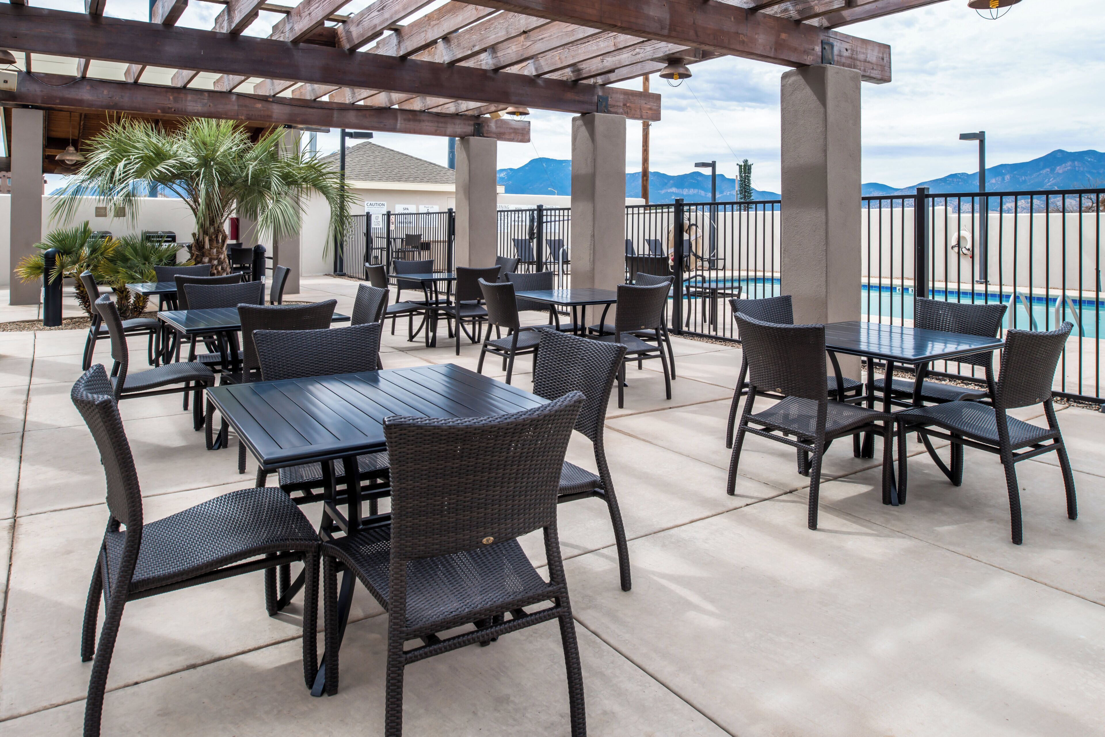 An outdoor patio area with tables and chairs, a pool, and mountains in the background.