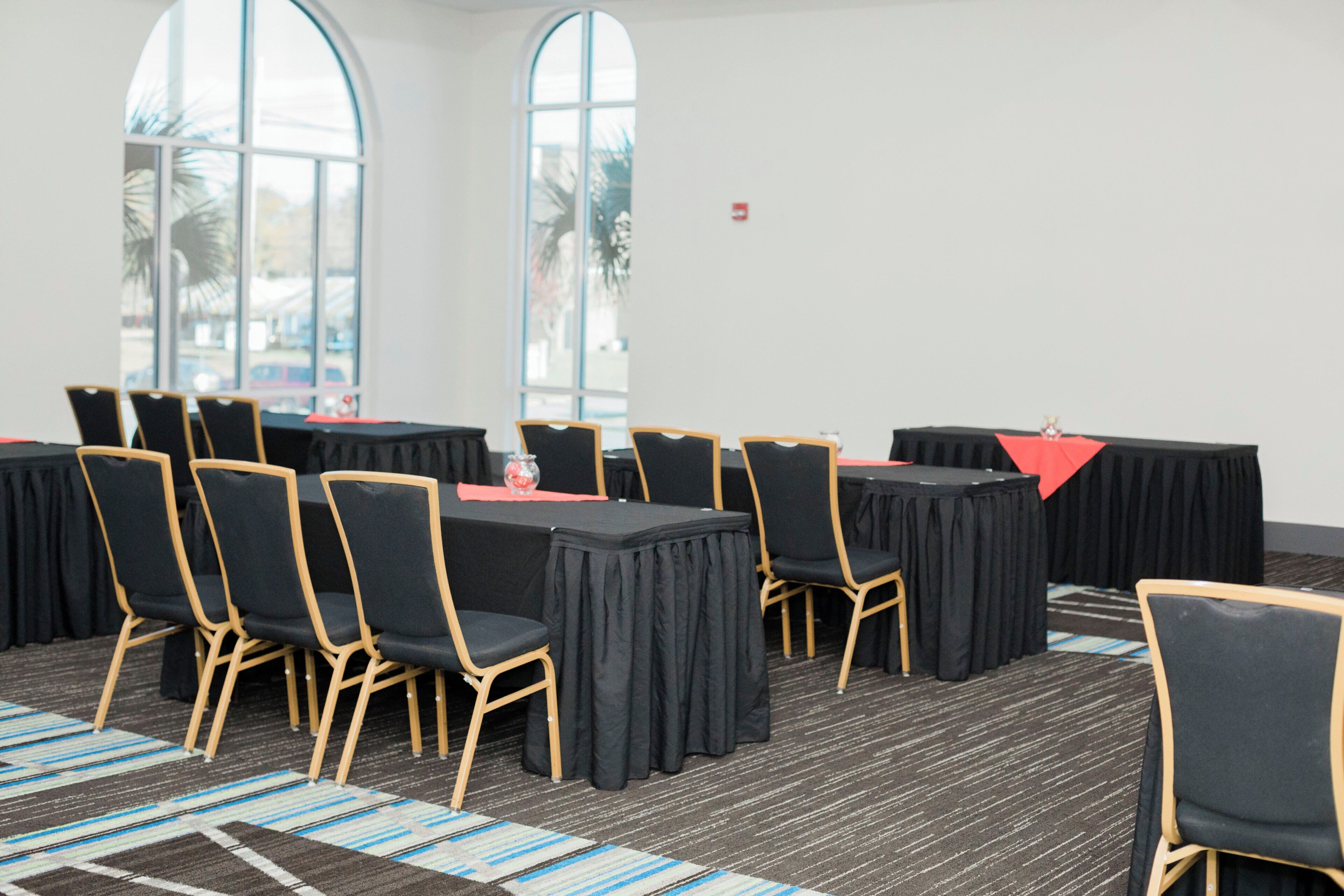 A conference room with tables and chairs, large windows, and a carpeted floor.