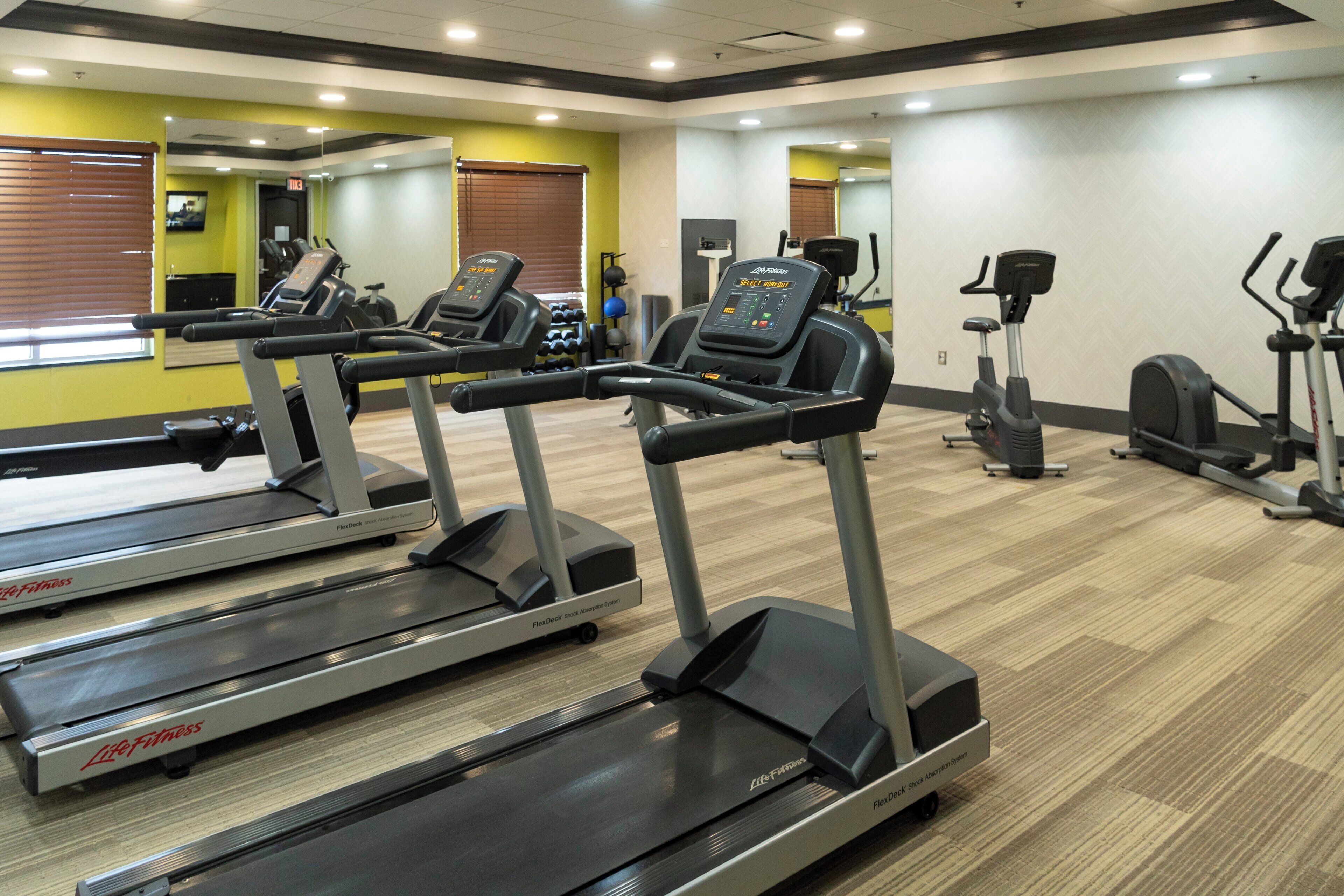 Un gimnasio con cintas de correr, bicicletas estáticas y un espejo grande.