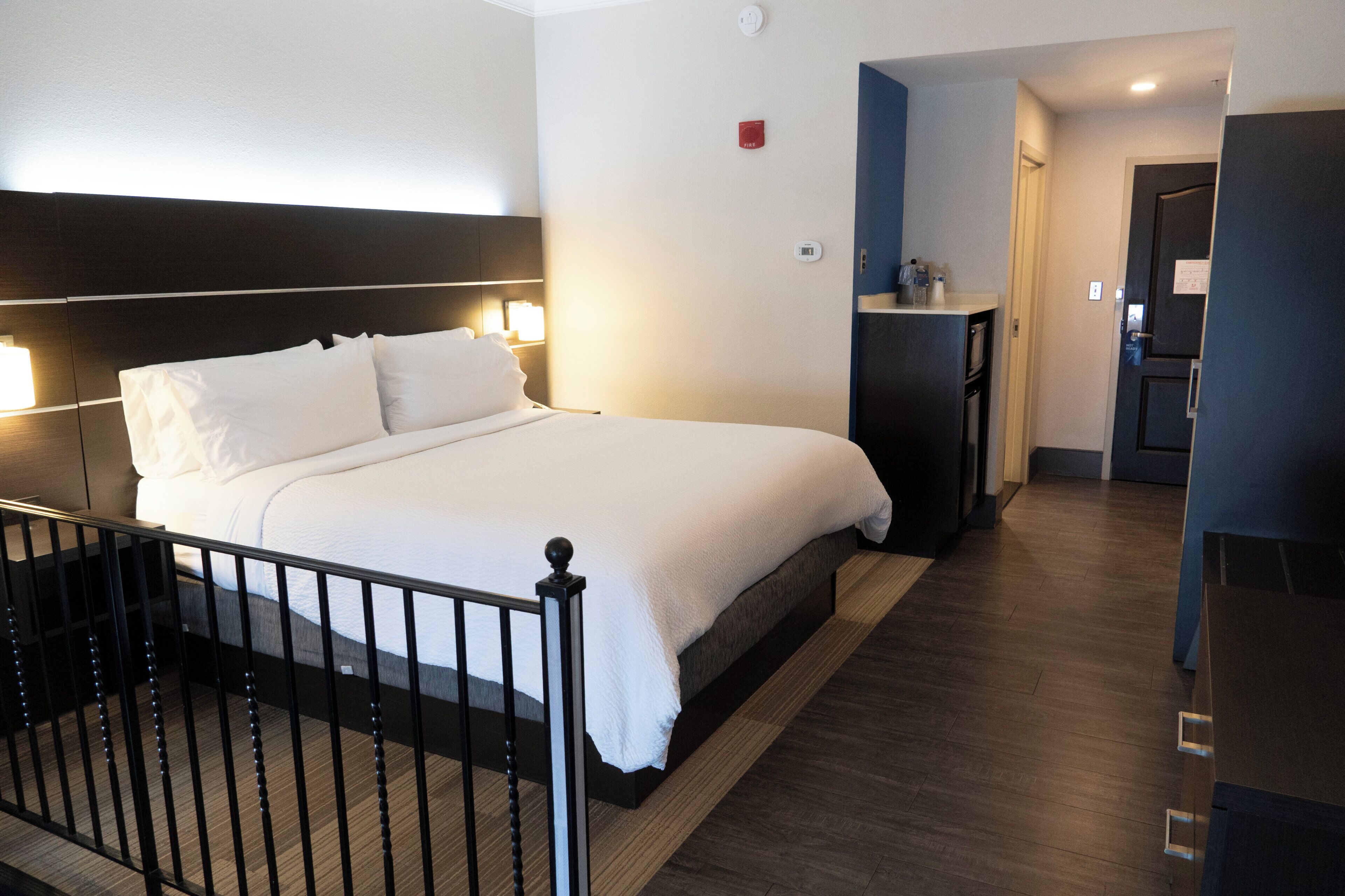 Una habitación de hotel con cama, mesita de noche y una pequeña cocina.