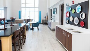 A modern kitchen with a dining area, large windows, and a wall-mounted dish display. - Holiday Inn Express & Suites Columbia-Fort Jackson by IHG (Columbia)