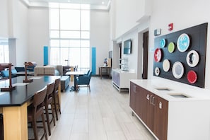 A modern kitchen with a dining area, large windows, and a wall-mounted dish display. - Holiday Inn Express & Suites Columbia-Fort Jackson by IHG (Columbia)